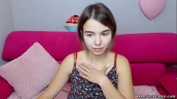 Little brunette amateur teen in summer colorful dress sitting on pink couch and posing and chatting with users of her homemade private webcam show